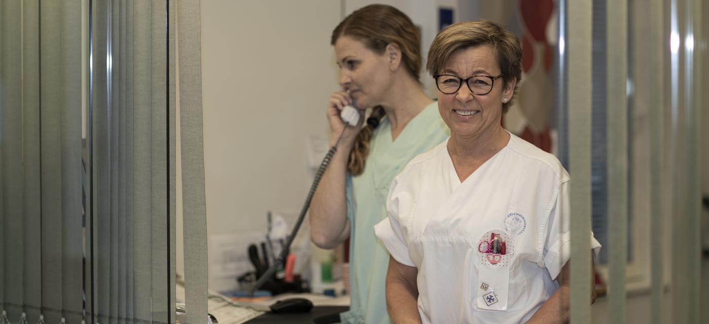 Sjukskötare tar emot i receptionslucka. En annan står i bakgrunden med telefon.