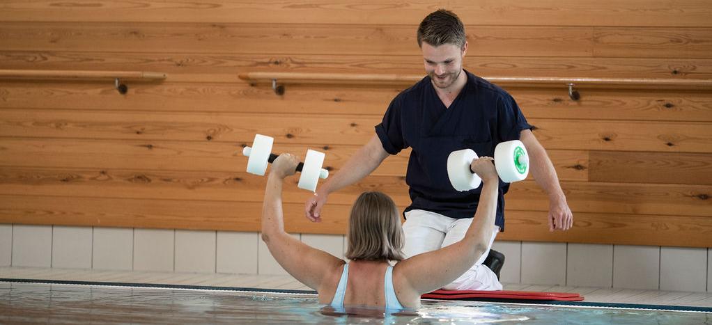 En fysioterapeut instruerar en patient som lyfter hantlar i en bassäng.