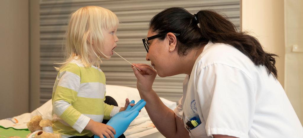 En läkare tittar en liten flicka i munnen.