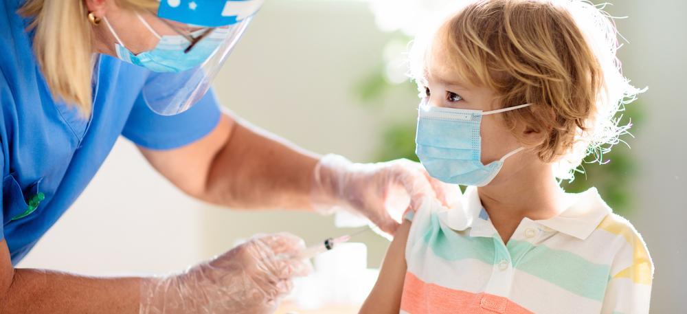 Barn med mask blir vaccinerat av sjukskötare med visir