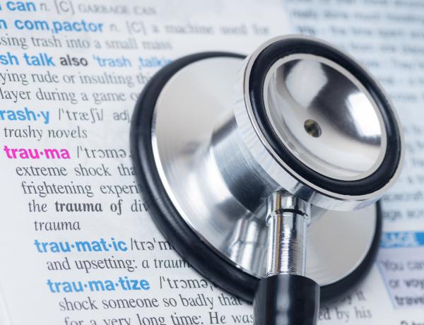 ett stetoskop i förgrunden och en ordbok i bakgrunden där ordet trauma är markerat 